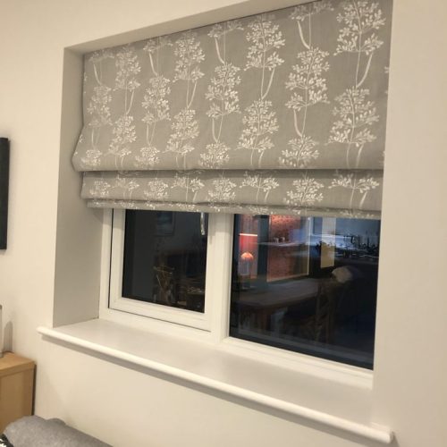 Grey botanical print roman blind above a window beside a dark sofa