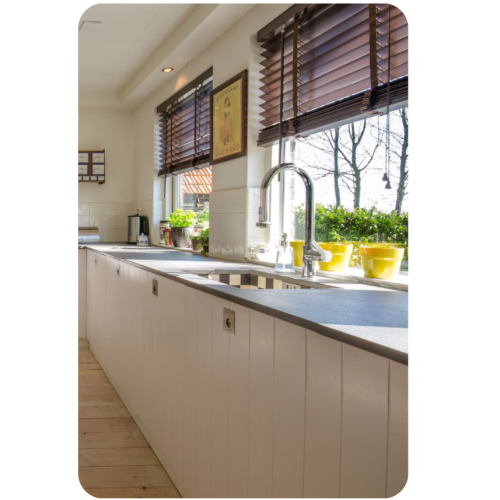Wooden venetian blinds above a kitchen sink window with potted plants