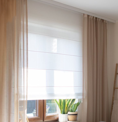 Sheer white roman blind layered with tan curtains beside a sunlit window